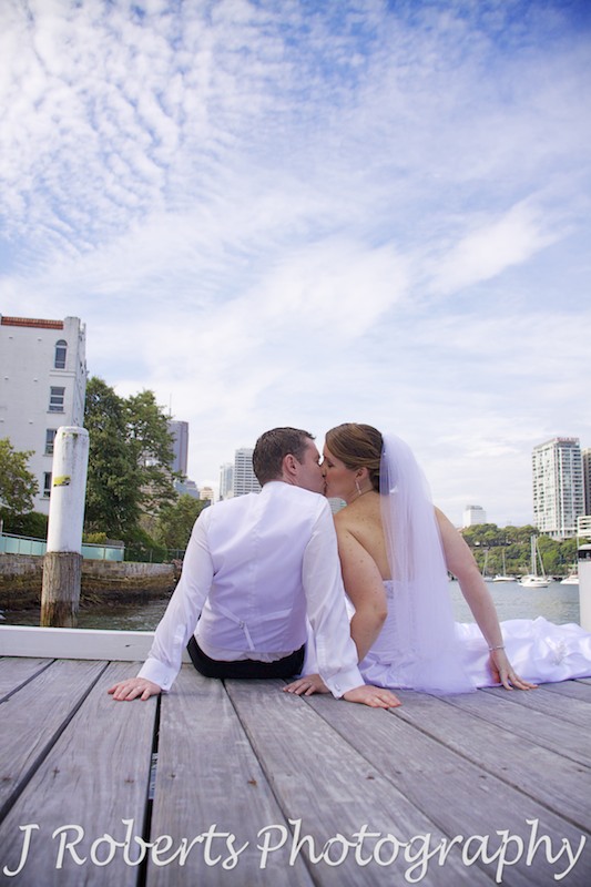 Bride and groom sitting on pier kissing - wedding photography sydney